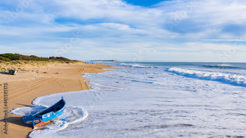 Immigrant and refugee dinghy boat stranded on the shore of a bautiful sand beach in south Spain. Coast of Cadiz in Andalusia with wooden boat washed by the shore waves photo