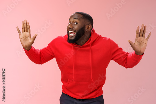 Knock who there. Charming happy funny black bearded guy bending towards camera raised palms move like mime act pressed face glass smiling joyfully fool around playful energized mood