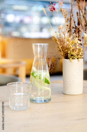 Water with lemon and cucumber in a glass bottle. Sassy water for detox or diet on a wooden table in a cafe. Healthy food, weight loss, lifestyle concept