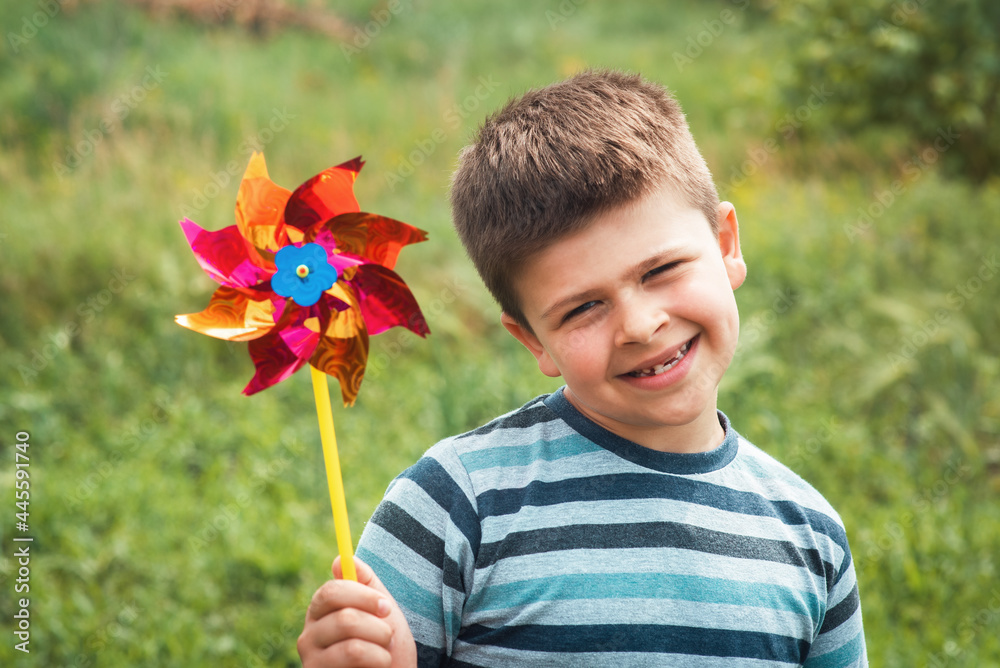A portrait of a lucky sweet boy holding a flywheel in a park. Kid's holding a game with a windmill A portrait of a lucky sweet boy holding a flywheel in a park. Kid's holding a game with a windmill