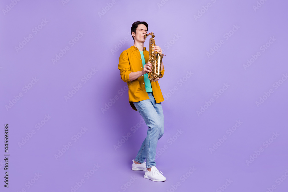 Full body photo of cool brunet young guy play sax wear brown shirt jeans isolated on violet color background Full body photo of cool brunet young guy play sax wear brown shirt jeans isolated on violet color background