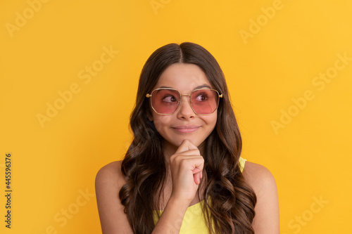 happy dreamy kid in summer glasses has curly hair on yellow background, hairstyle