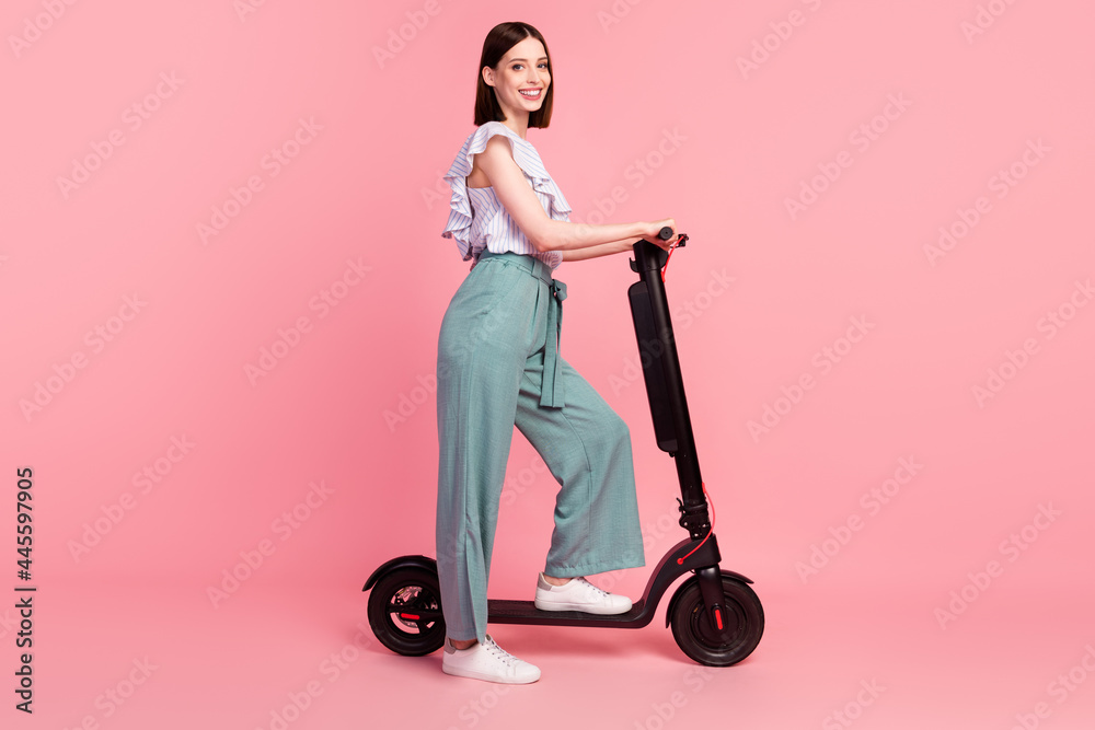 Full length profile side photo of young girl happy positive smile weekend ride eco scooter isolated over pink color background