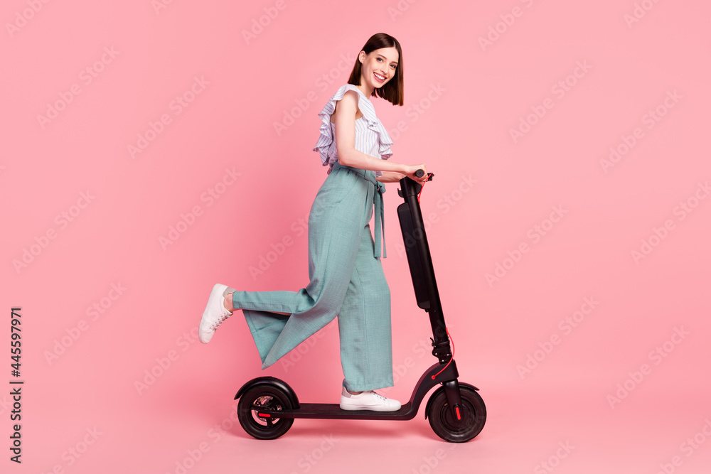 Full size profile side photo of young girl happy positive smile driver trip weekend scooter isolated over pink color background Full size profile side photo of young girl happy positive smile driver trip weekend scooter isolated over pink color background
