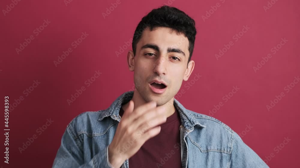 A brunette man is yawning while looking to the camera standing isolated over red background in the studio A brunette man is yawning while looking to the camera standing isolated over red background in the studio