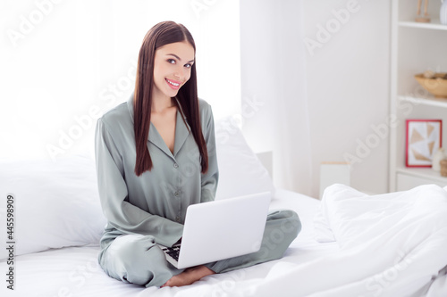 Photo of charming pretty young lady grey sleepwear sitting legs crossed chatting modern gadget smiling indoors room home house