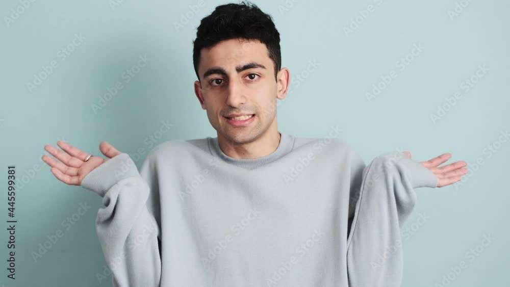 A confused man is shrugging shoulders standing isolated over blue background in the studio A confused man is shrugging shoulders standing isolated over blue background in the studio