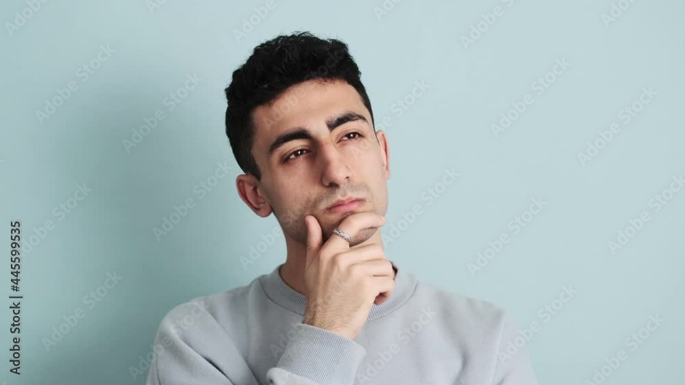 A serious man is thinking about something standing isolated over blue background in the studio A serious man is thinking about something standing isolated over blue background in the studio