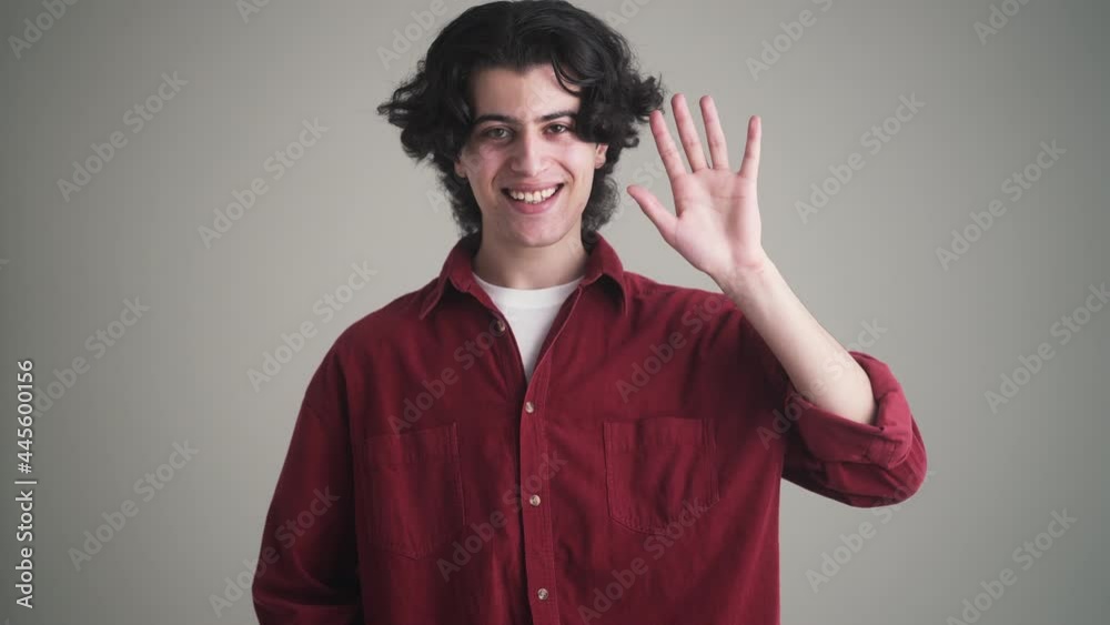 A happy man in red shirt is doing hello gesture standing isolated over grey background in the studio A happy man in red shirt is doing hello gesture standing isolated over grey background in the studio
