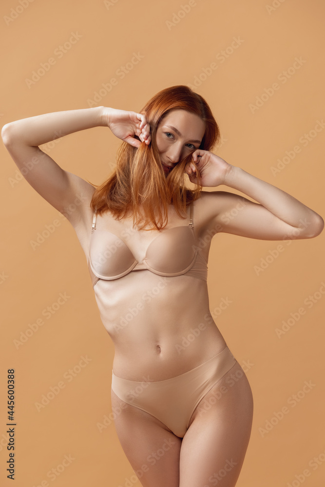 Obraz premium Perfect slim tanned young woman in lingerie posing isolated over sand color studio back ground. The fitness, diet, sports, natural beauty and aesthetic cosmetology concept.