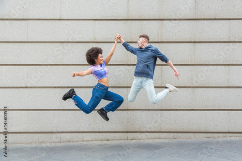 Caucasian man and afro woman jumping at the same time bumping hands with blue cassul clothes