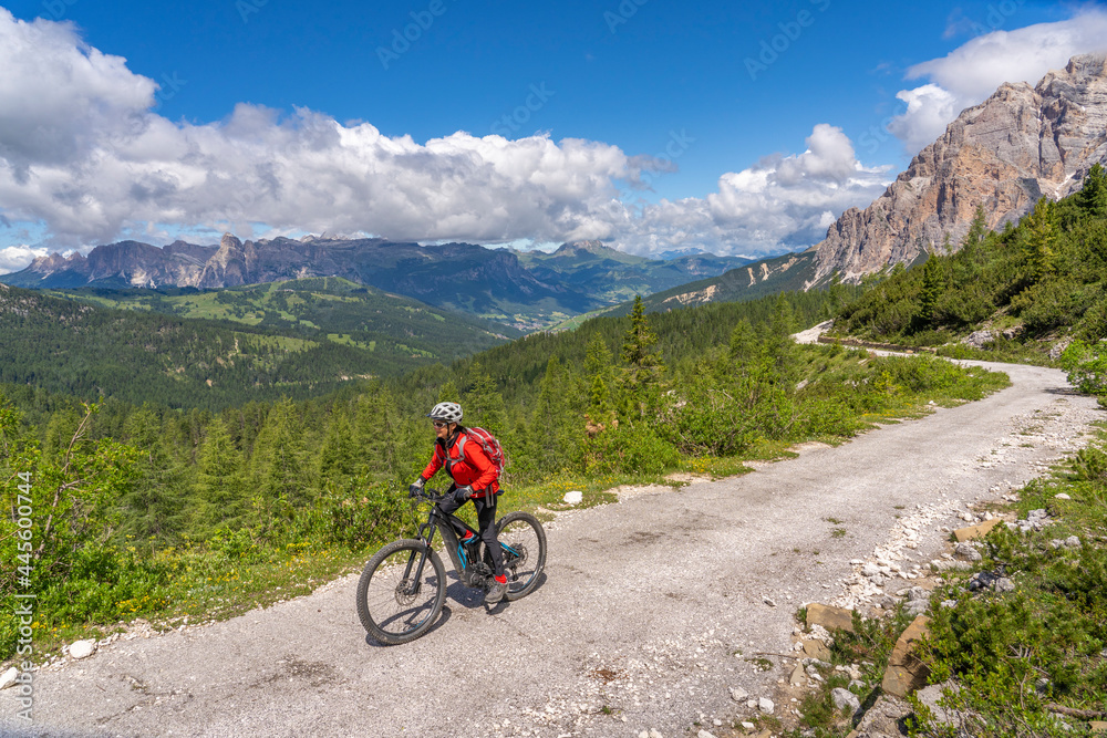 pretty active senior woman riding her electric mountain bike up to Valparola Pass in the Alta Badia Dolomites , South Tirol and Trentino, Italy