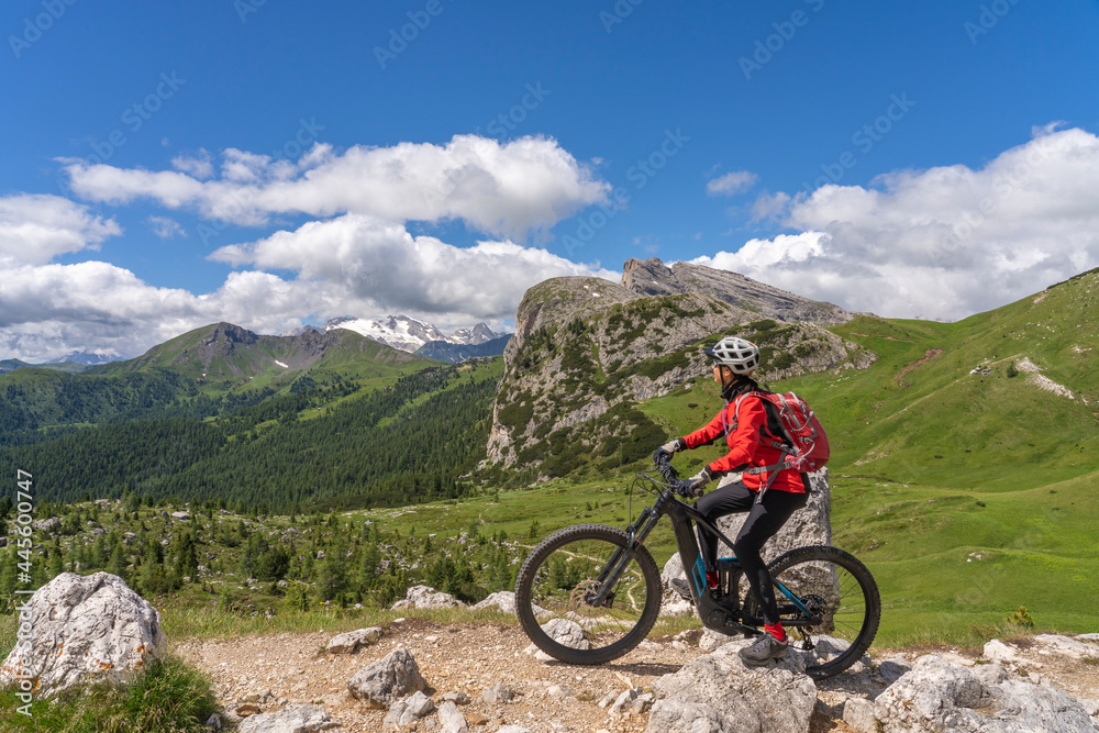 pretty active senior woman riding her electric mountain bike up to Valparola Pass in the Alta Badia Dolomites , South Tirol and Trentino, Italy