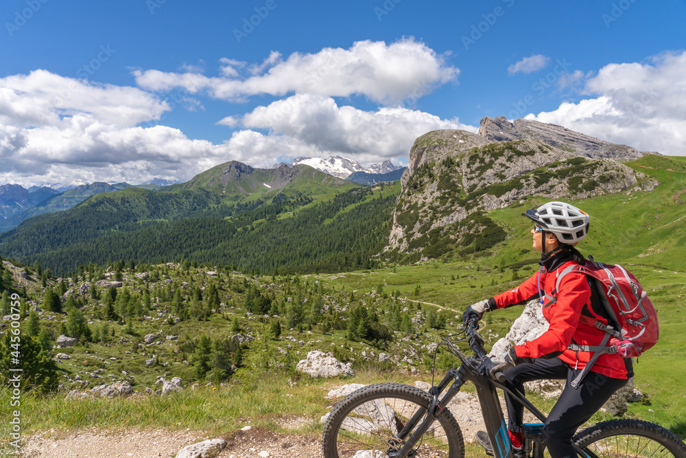pretty active senior woman riding her electric mountain bike up to Valparola Pass in the Alta Badia Dolomites , South Tirol and Trentino, Italy