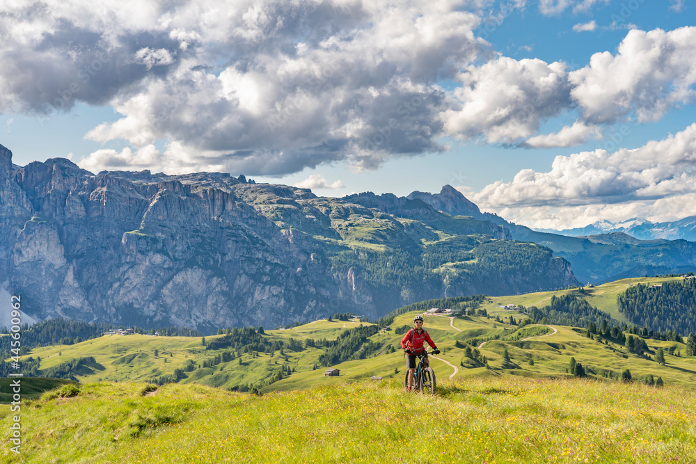 nice and active senior woman riding her electric mountain bike on the Pralongia Plateau in the Alta Badia Dolomites with mountains of Sella Group in Background, South Tirol and Trentino, Italy