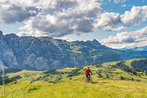 nice and active senior woman riding her electric mountain bike on the Pralongia Plateau in the Alta Badia Dolomites with mountains of Sella Group in Background, South Tirol and Trentino, Italy © Uwe