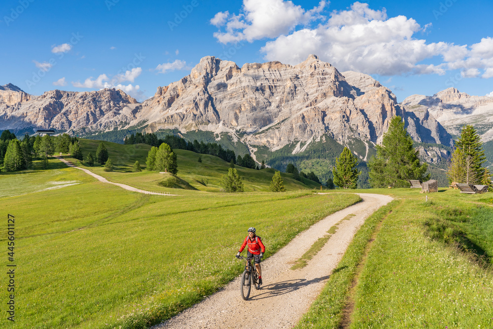 nice and active senior woman riding her electric mountain bike on the Pralongia Plateau in the Alta Badia Dolomites with awesome Sasso die Santa Cruce summit in Backg, South Tirol and Trentino, Italy