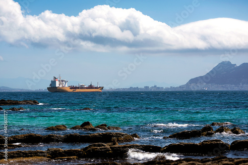 Vista de un gran buque de carga amarillo en la bahía de Algeciras y el Peñon de Gibraltar de fondo, Cádiz, Andalucía, España.