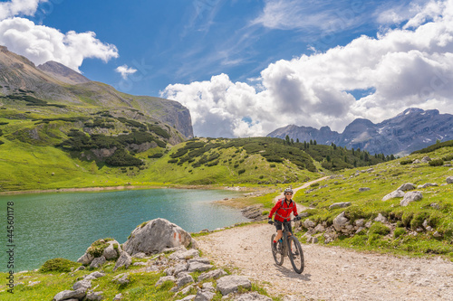 Fototapeta Naklejka Na Ścianę i Meble -  pretty active senior woman riding her electric mountain bike at Lago de in the Fanes high Valley, part of Fanes-Sennes-Braies nature park in the Alta Badia Dolomites,  South Tirol and Trentino, Italy
