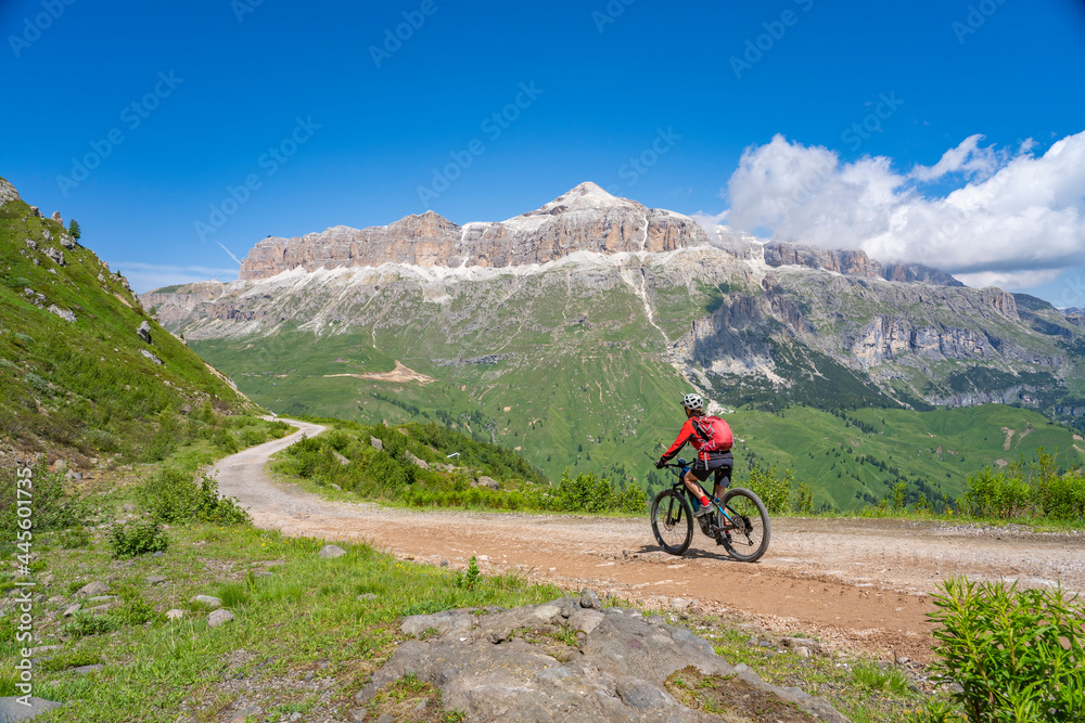 pretty active senior woman riding the famous Sella Ronda  mountain bike Trail  in Sella mountain group, Dolomites  of Selva Wolkenstein, Val Gardena, South Tirol and Trentino, Italy