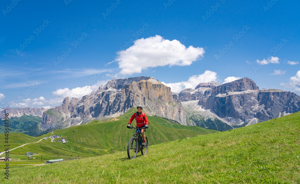 pretty active senior woman riding the famous Sella Ronda  mountain bike Trail  in Sella mountain group, Dolomites  of Selva Wolkenstein, Val Gardena, South Tirol and Trentino, Italy