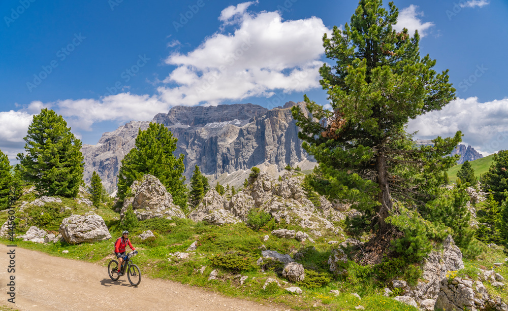 pretty active senior woman riding her electric mountain bike famous  Stone City below Sassolungo summit in Sella Dolomites  of Selva Wolkenstein, Val Gardena, South Tirol and Trentino, Italy