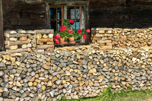 Kaminholz und Fenster mit roten Geranien photo