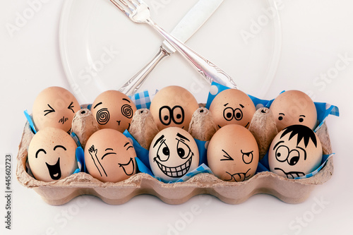 Easter eggs with different faces in eggbox and round plate with cutlery, knife and fork. Types of temperaments. Sanguine, choleric, angry, phlegmatic, happy or melancholic. Face illustrated on eggs photo