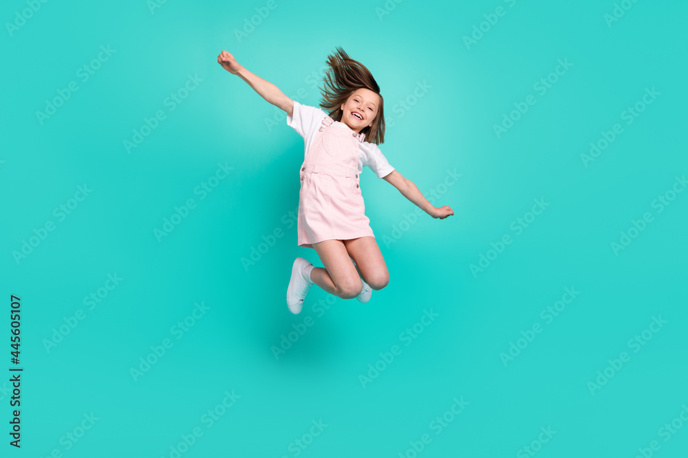 Photo of charming sweet school girl wear pink overall smiling jumping high arms sides isolated teal color background
