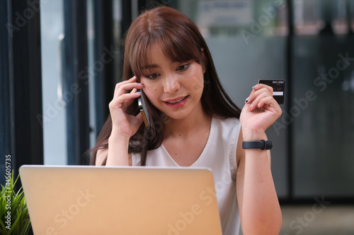 Front view with businesswoman talking on her phone and holding credit card while looking on laptop, Business and finance concept.