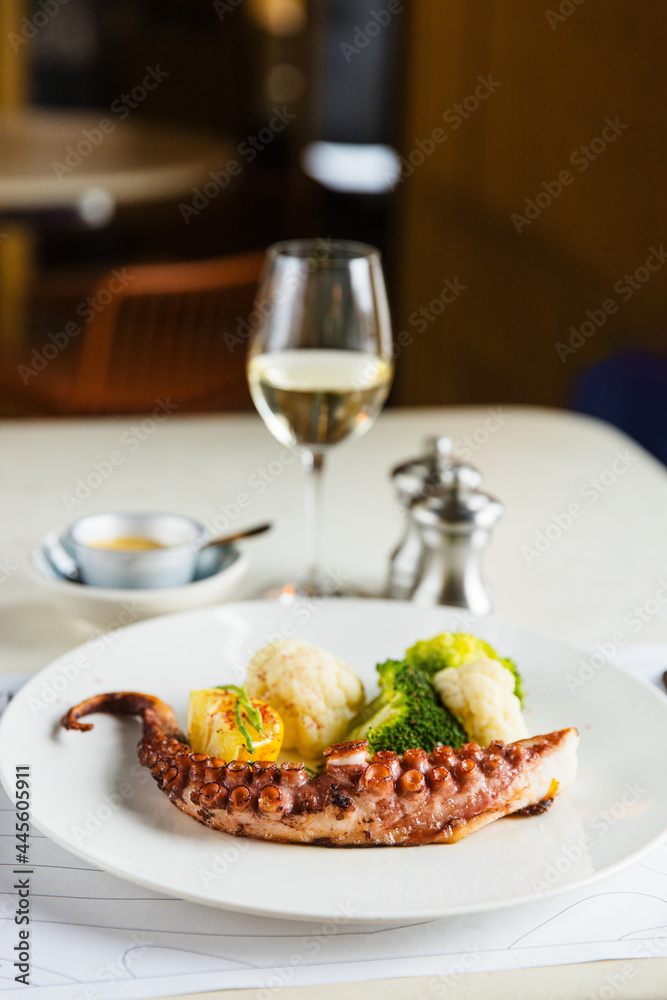 Fried octopus tentacle with broccoli and cauliflower, on a white plate, with white wine