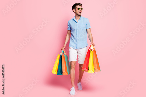 Photo of man walk carry store bags look empty space wear sunglass blue shirt isolated on pink color background