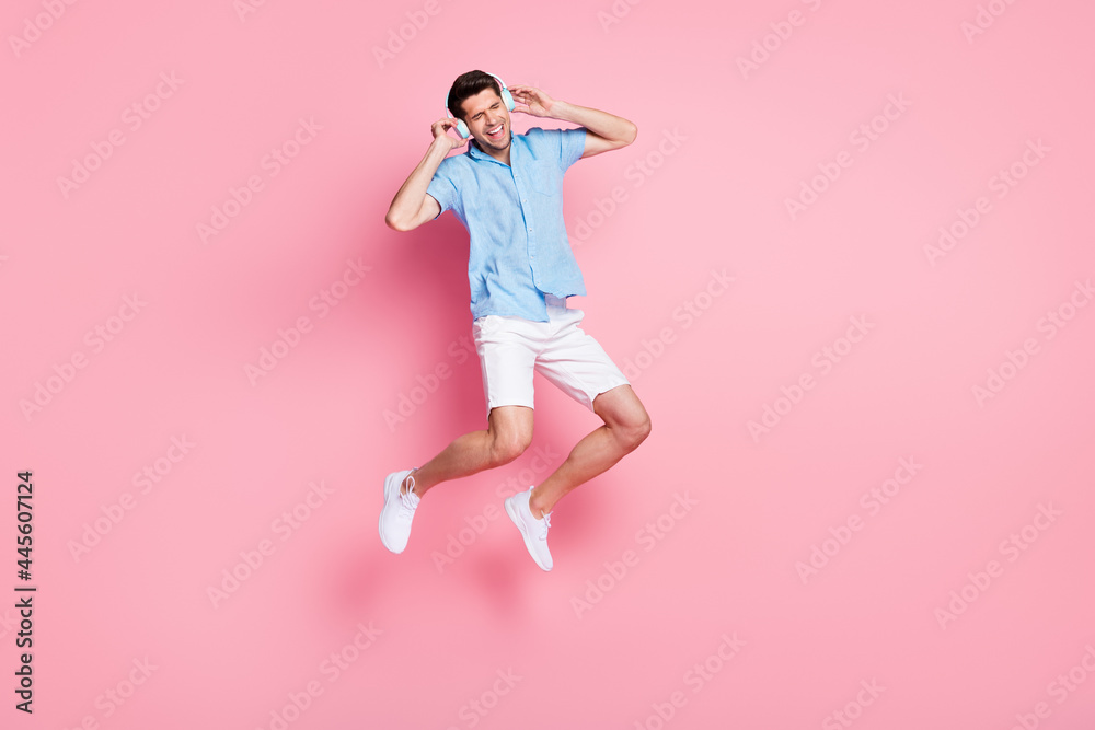 Full length body size photo man listening music in headphones jumping up isolated pastel pink color background