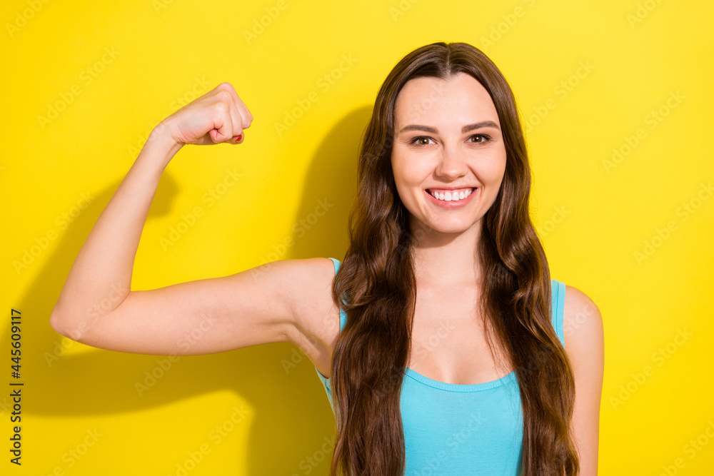 Portrait of attractive cheerful girl demonstrating strong muscles isolated over bright yellow color background