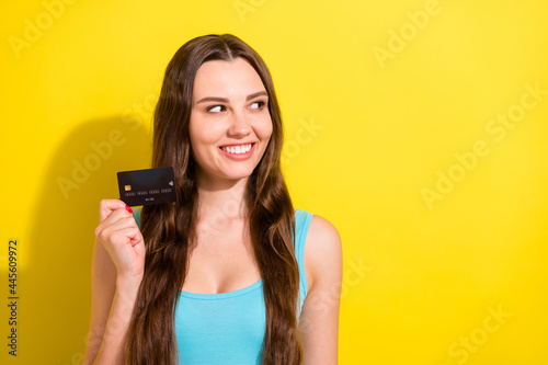 Photo portrait girl wearing blue singlet smiling showing bank card looking copyspace isolated vibrant yellow color background