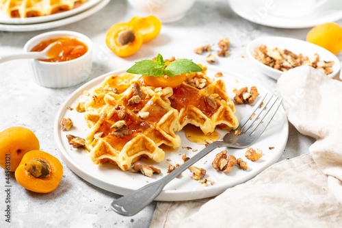 Traditional classic Belgian or Brussels waffles with apricot jam and walnuts in a ceramic plate on a light gray kitchen table closeup
