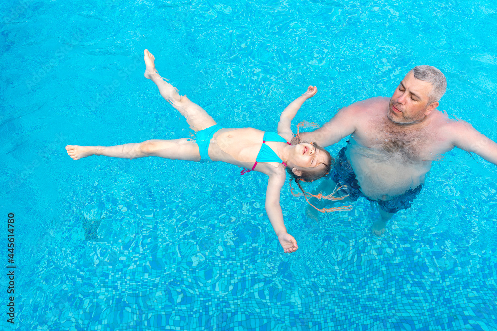 dad and little daughter swim in the pool on summer vacation