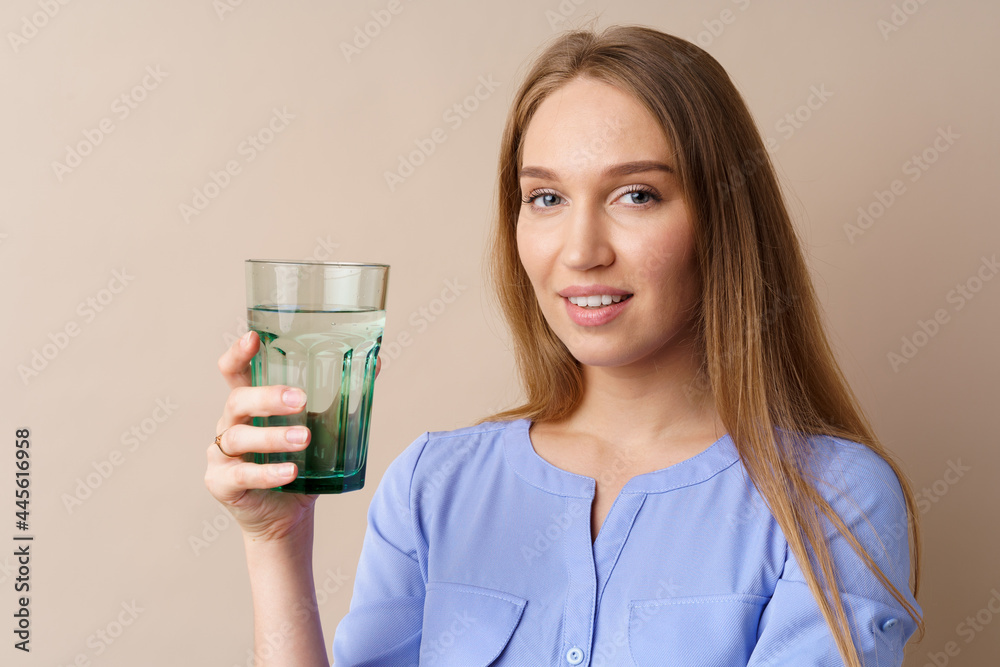 Beautiful healthy young woman drinking water from a glass on beige background Beautiful healthy young woman drinking water from a glass on beige background