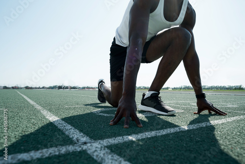 Photo below. African American athlete man preparing for the race at the competition standing at the start
