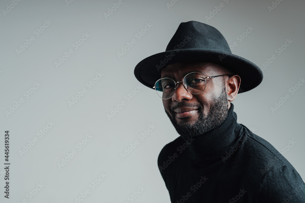 Photo from the side. Handsome cute african american man wearing hat and glasses smiling looking at camera