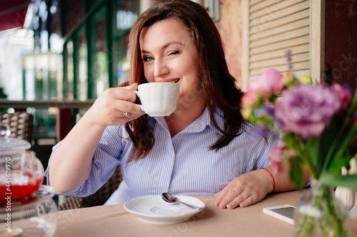 A beautiful woman drinks tea on the summer veranda in the cafe