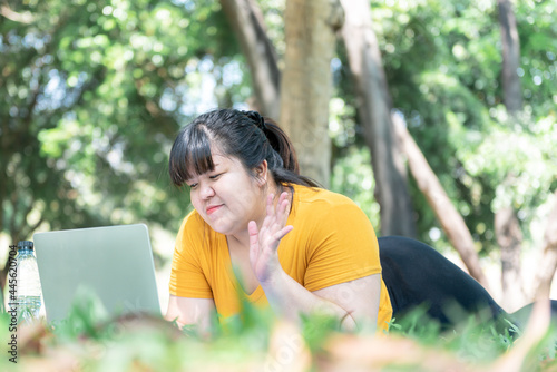 Asian attractive fat woman lying on the lawn to relax And smile with happiness While using, looking a notebook computer, to people and relaxation with nature concept.