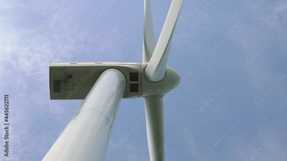 Contemporary windmill blades rotate as alternative energy source under sky with white clouds on summer day low angle shot. Environment conservation concept. Contemporary windmill blades rotate as alternative energy source under sky with white clouds on summer day low angle shot. Environment conservation concept.