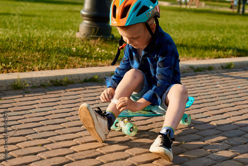 A small five-year-old boy in a helmet fell off a skateboard, injured his leg and is sealing it with a plaster