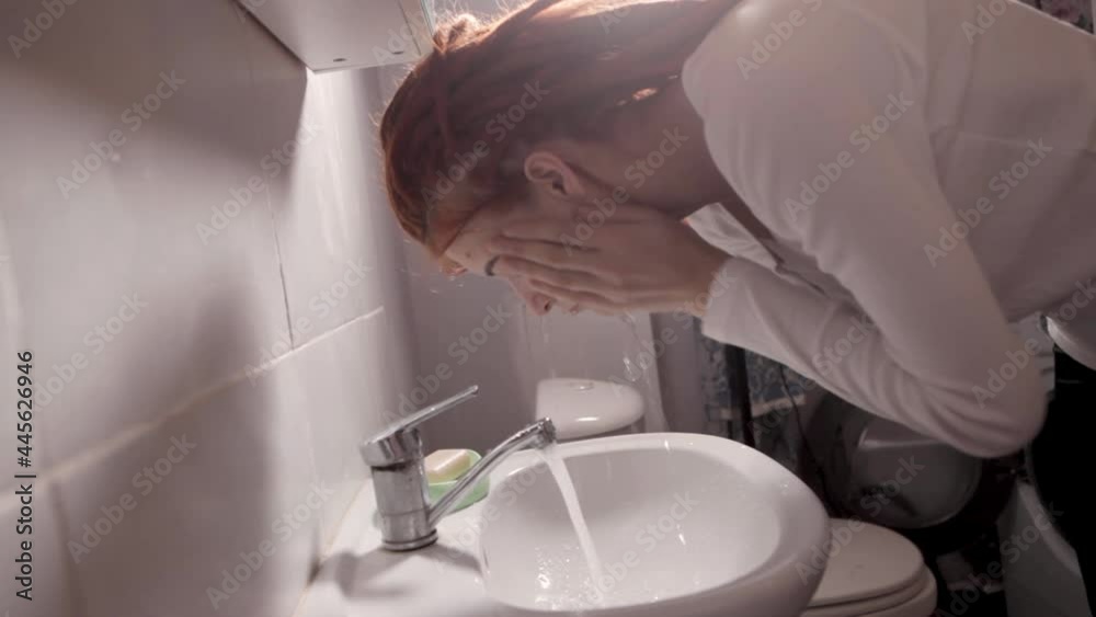 A woman washes her face. Daily hygiene procedures. A red-haired girl with dreadlocks takes care of her face. Beautiful young woman washing her face splashing water in a home bathroom. A woman washes her face. Daily hygiene procedures. A red-haired girl with dreadlocks takes care of her face. Beautiful young woman washing her face splashing water in a home bathroom.