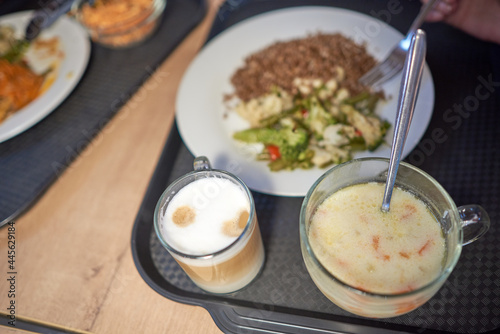 Healthy lunch in a cafe on a tray - milk soup, buckwheat with vegetables, a glass of cappuccino