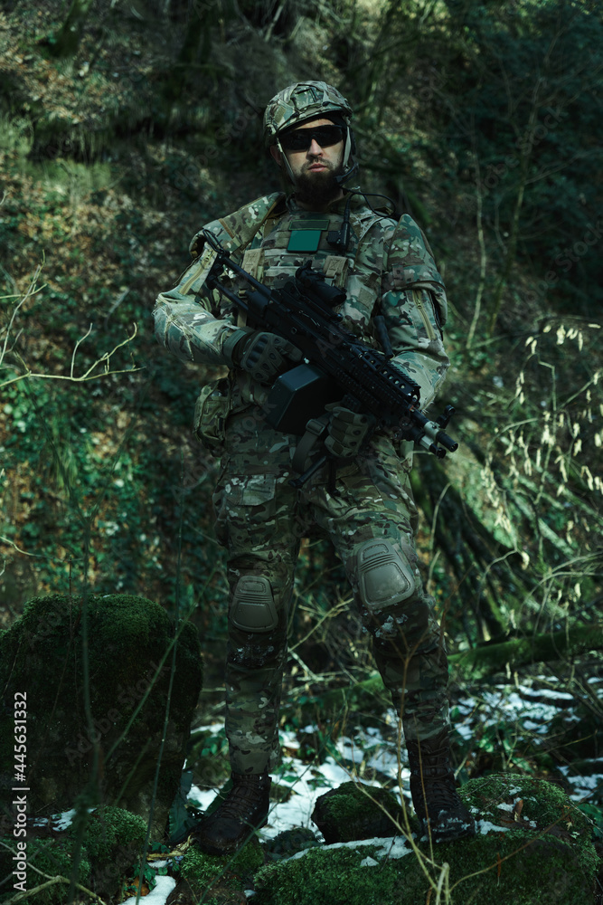 Portrait of airsoft player in professional equipment with machine gun in the forest. Soldier with weapons at war