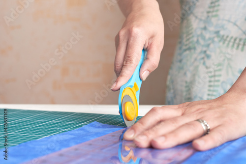 Home craft concept photo - woman hands, cutting textile for patchwork or quilt  on a mat with rotary cutter and ruler.