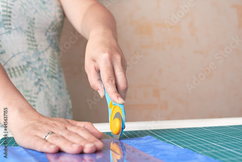 Home craft concept photo - woman hands, cutting textile for patchwork or quilt  on a mat with rotary cutter and ruler.