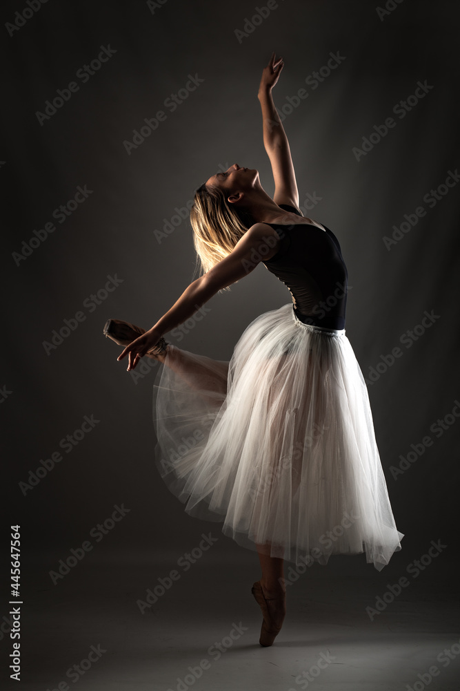 Fototapeta premium ballerina with a white dress and black top posing on gray background.